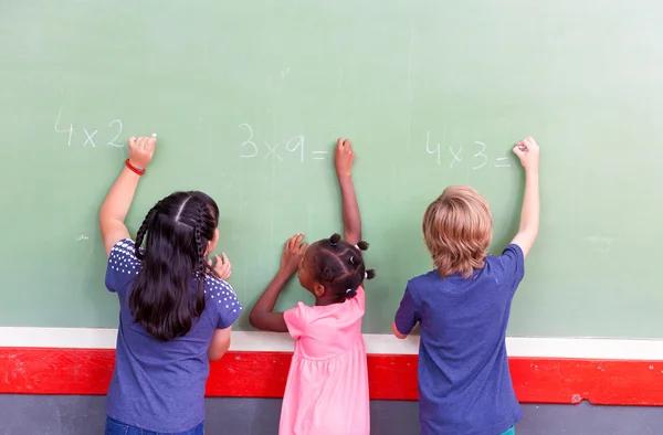 Mixed race school children writing on chalkboard — Stock Photo, Image