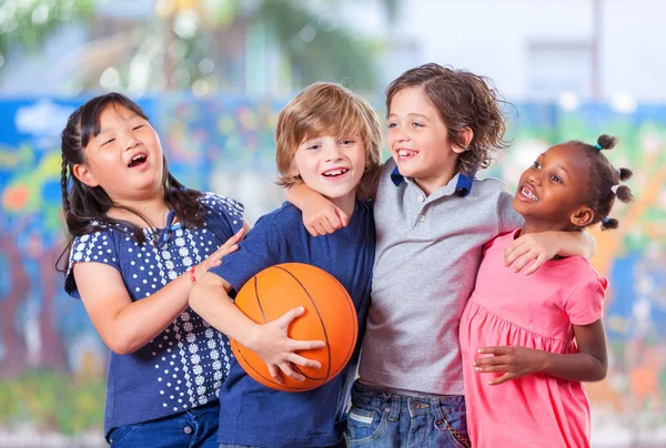 Happy children embracing while playing basketball. Primary schoo — Stock Photo, Image