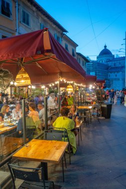 Pisa, İtalya - 12 Temmuz 2025: Pisa 'daki kalabalık restoran terası gece görüşü ve yaz atmosferinde gezginler açık havada yemek yiyor.