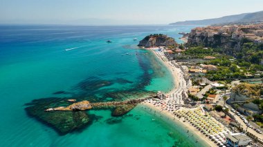 Tropea plajı güneşlenenlerle, şemsiyelerle ve sıcak bir günde dalgalarla görüldü..