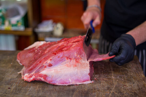 Close-up of expert butcher slicing beef with sharp knife on workbench.