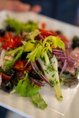 Renkli sebzeler ve yeşilliklerle dolu bir restoranda servis edilen taze karışık salata..