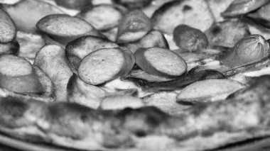 Taze pişmiş pizza sosisi eritilmiş peynirle sunuluyor ve zengin lezzetli malzemeler detaylıca sunuluyor, siyah ve beyaz görünüm.