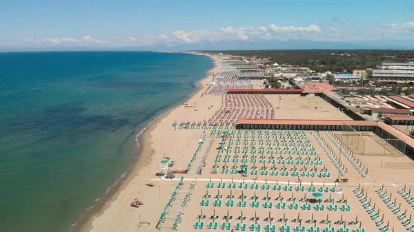 Yaz mevsiminde sıralı şemsiyeler ve güneşli yataklı bir sahil beldesinin havadan aşağı manzarası..