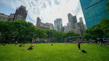 New York Şehri - 12 Haziran 2025: Sıcak ve güneşli bir yaz gününde Bryant Park 'ta çimlerin üzerinde dinlenen turistler.