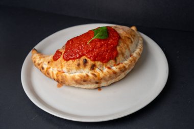 Siyah arka planda izole edilmiş Calzone pizzası dramatik ışıklandırma ve İtalyan mutfağı kavramı.