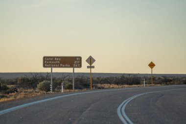 Avustralya yol tabelaları, Batı Avustralya 'daki Kuzey Batı Sahil Otobanı boyunca uzanan ve mavi gökyüzü olan Coral Bay' e doğru ilerliyor..