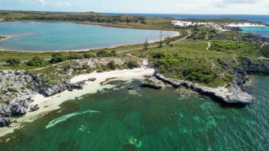 Rottnest Adası sahil şeridinin panoramik manzarası berrak suları ve güneş ışığında el değmemiş plajı gösteriyor..