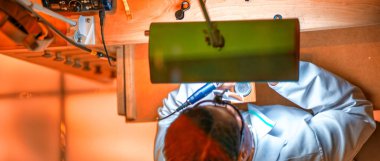 Bir saat atölyesinin aşağı bakan görüntüsü. Saatçi kol saatini tamir ediyor..