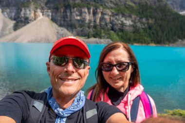 Mutlu çift, turkuaz su ve dağlarla çevrili Moraine Gölü 'nün tadını çıkarıyor..