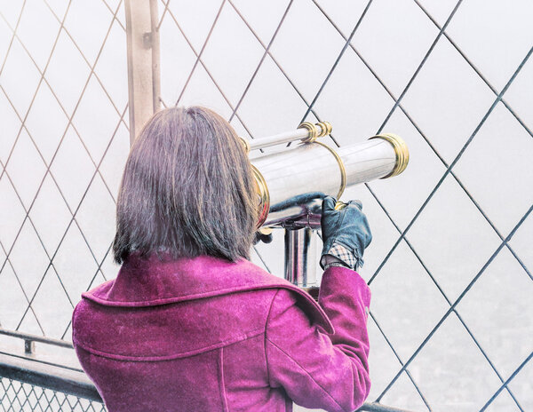 Vintage back view of a woman looking in city telescope.