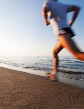 Bir kumsalda güneş doğarken koşan genç adam. Motion blur efekti. Kavramlar: su kuyusu-varlık, canlılık, sağlıklı yaşam, tatil, spor, eğitim