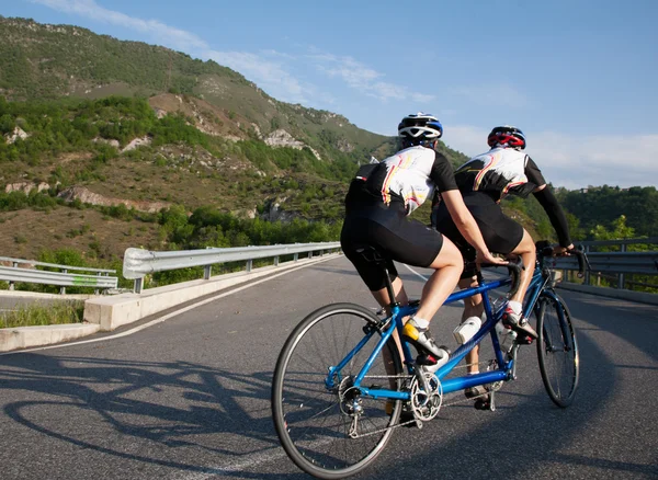 Ciclistas en una bicicleta en tándem montando cuesta arriba en una carretera de montaña — Foto de Stock