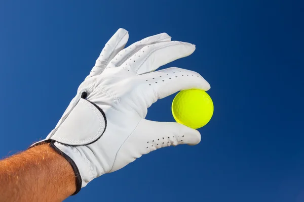 Mão usando luva de golfe segurando uma bola de golfe amarelo — Fotografia de Stock