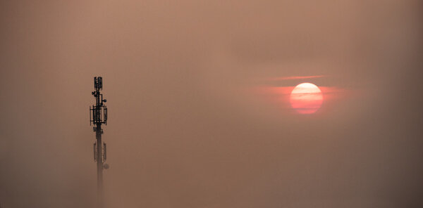 Mobile phone antenna tower emerges from the fog over a sunset sk