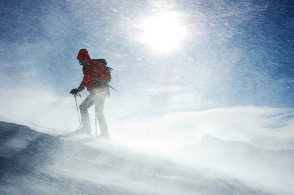 Одинокий лыжник, поднимающийся на вершину горы во время снежной бури — стоковое фото