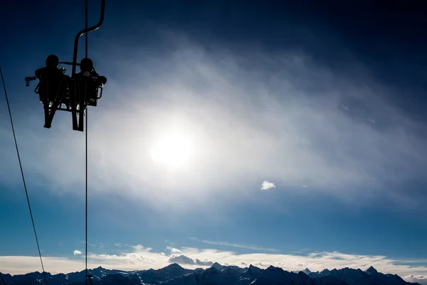 Två skidåkare i en stollift bakgrundsbelyst av solen. — Stockfoto