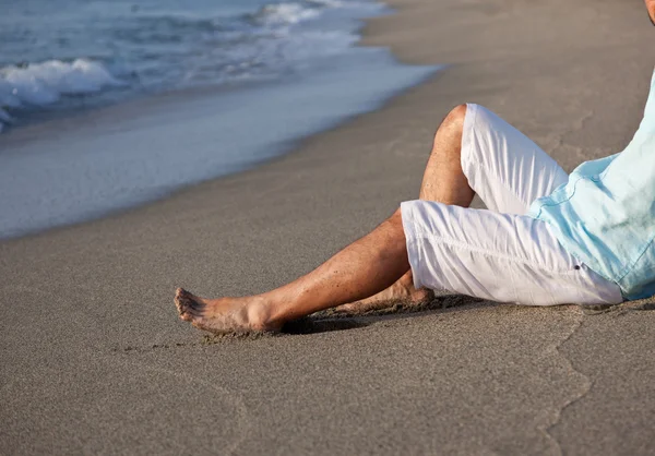 Man sitter på stranden i sunrise ljus. — Stockfoto