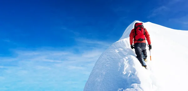 L'alpiniste arrive au sommet d'un pic enneigé. Concepts : détermination, courage, effort, réalisation de soi. Ciel dégagé, journée ensoleillée, saison hivernale. Grand espace de copie à gauche . — Photo