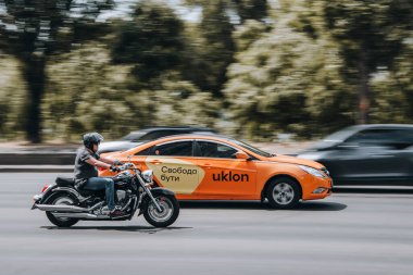 Ukrayna, Kyiv - 27 Haziran 2021: Suzuki Davetsiz misafir motosikleti Hyundai Sonata Uklon Taksi aracı yolda ilerliyor. 