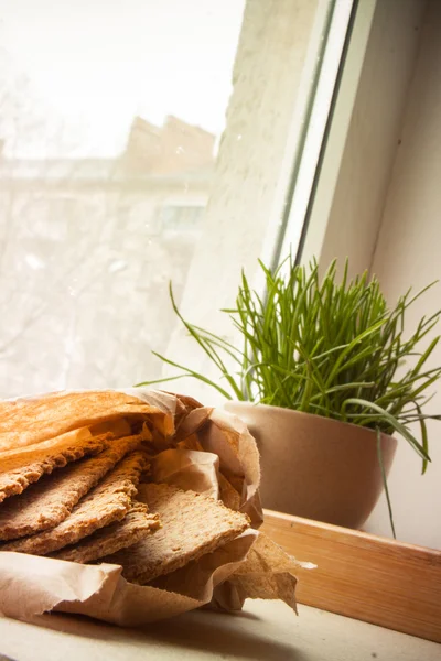 Tray with crispbreads and cup of grass  on the window sill — Stock Photo, Image