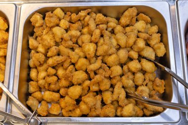 Isırık büyüklüğünde kızarmış tavuk parçalarıyla dolu büyük metal bir tepsinin yakın çekim görüntüsü. Açık büfe veya restoranda servis edilmeye hazır.