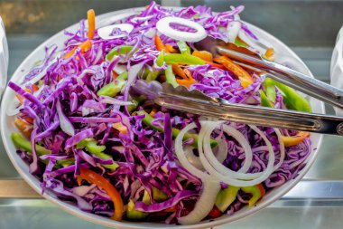 Canlı ve renkli lahana salatası dilimlenmiş kırmızı lahana, dilimlenmiş dolma biber ve soğan halkaları maşayla servis edilmeye hazır.