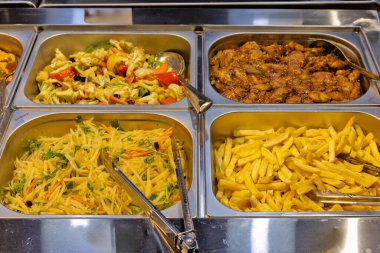 Açık büfe servis hattının yakın çekim görüntüsü. Dört metal tepsi ile çeşitli yiyecek öğeleri seçmeye hazır.