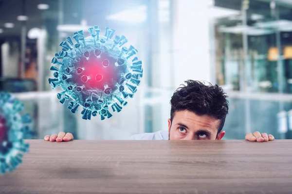 De man is bang voor het Covid19 virus en hij zit verborgen achter een bureau. — Stockfoto