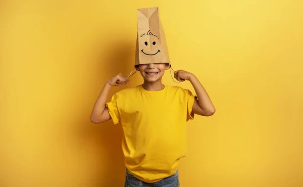 Barnet gömmer huvudet i en shoppingpåse. gul bakgrund — Stockfoto