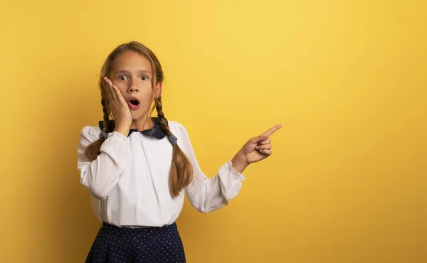 Young student is with shocked expression and indicates something. Yellow background. — Stock Photo, Image