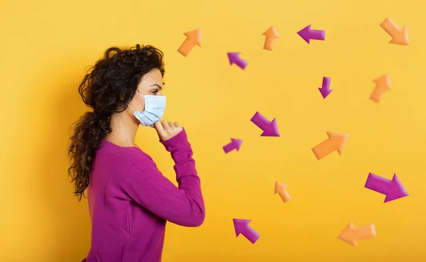 Girl with face mask is undecided about the arrow to follow. Concept of covid-19 confusion. Yellow background — Stock Photo, Image