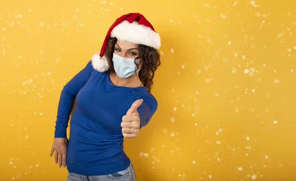 Frau mit Weihnachtsmütze blickt optimistisch auf die Niederlage gegen das Covid 19 Coronavirus. gelber Hintergrund. — Stockfoto