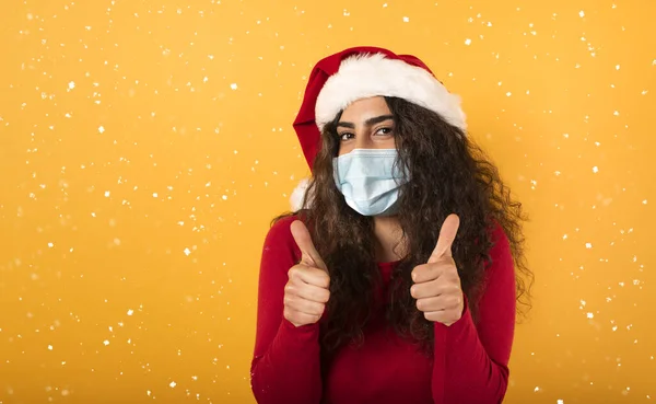 Frau mit Weihnachtsmütze blickt optimistisch auf die Niederlage gegen das Covid 19 Coronavirus. gelber Hintergrund. — Stockfoto