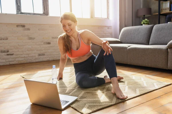 Young woman follows with a laptop a gym exercises. She is at home due to coronavirus codiv-19 quarantine — Stock Photo, Image