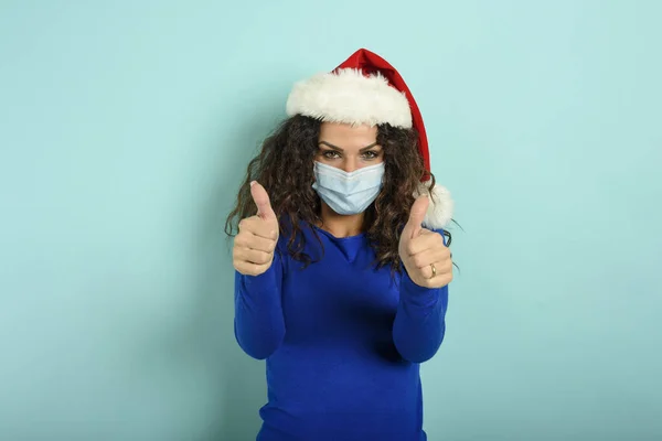 Mädchen mit Weihnachtsmütze ist optimistisch über den Sieg über das covid 19 Coronavirus. Cyan-Hintergrund. — Stockfoto