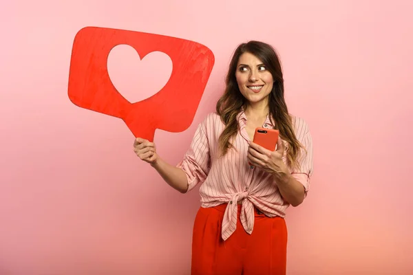 La femme est heureuse parce qu'elle reçoit des cœurs sur les réseaux sociaux. Fond rose — Photo