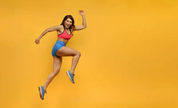Sport woman runs on yellow background. Happy and joyful expression. — Stock Photo, Image