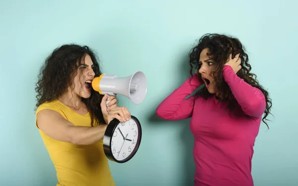 Una donna urla con un altoparlante ad un amico perché è troppo tardi. espressione arrabbiata. sfondo ciano — Foto Stock