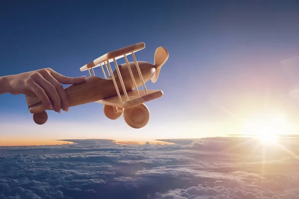 Gros plan d'un avion jouet vintage en bois, tenu par une main, volant au-dessus des nuages dans le ciel — Photo