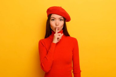 Kadın, eli sessiz olduğunu gösterir. Sarı arkaplan