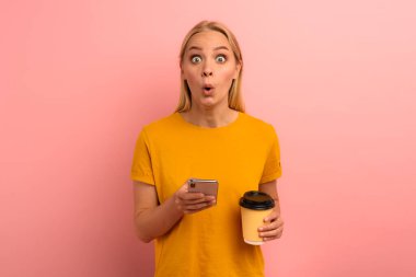 Sarışın, tatlı kız akıllı telefonuyla bir mesaj yazıyor. Mutlu ve şaşırmış yüz ifadesi. Pembe arkaplan