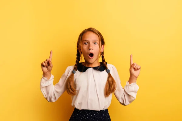 Young student is with shocked expression and indicates something. Yellow background — Stock Photo, Image