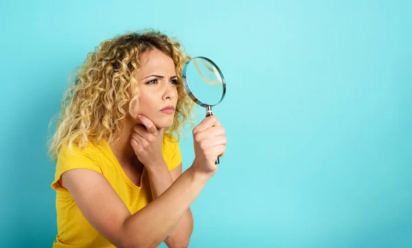 Menina com lente de aumento é desconfiado sobre algo. Contexto ciano — Fotografia de Stock