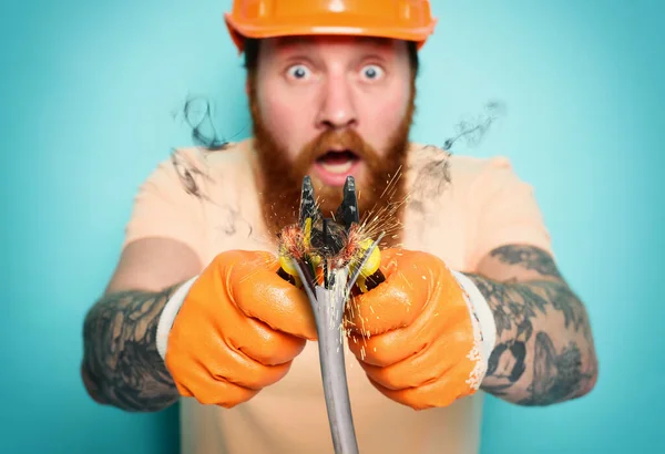 Incompetent worker electrician is unsure about his work. cyan background — Stock Photo, Image