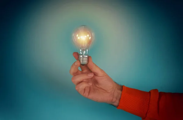 O homem segura uma lâmpada na mão. conceito de criatividade e solução. fundo ciano — Fotografia de Stock