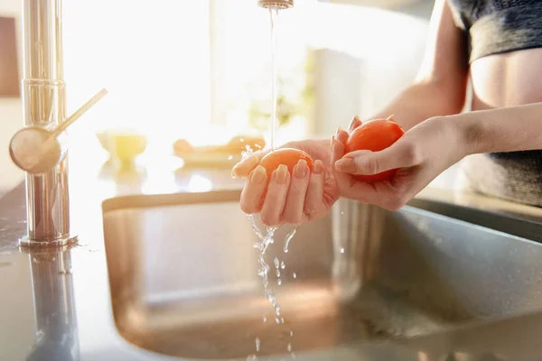 Fitness woman rinses fresh tomato in the sink — Stockfoto