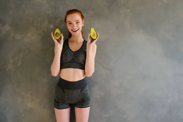 Chica atlética con ropa de gimnasio come aguacate en casa —  Fotos de Stock