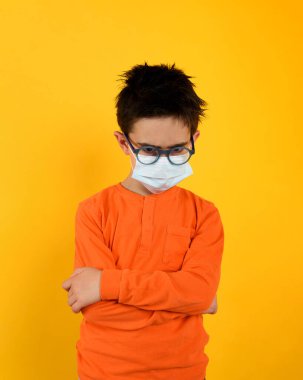 Covid-19 Coronavirus için yüz maskesi takmış mutsuz bir çocuğun portresi. sarı arkaplan