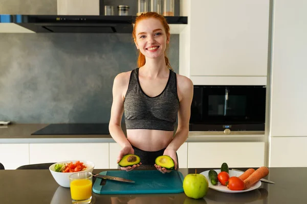 Spor elbiseli atletik kadın mutfakta meyve yiyor. — Stok fotoğraf